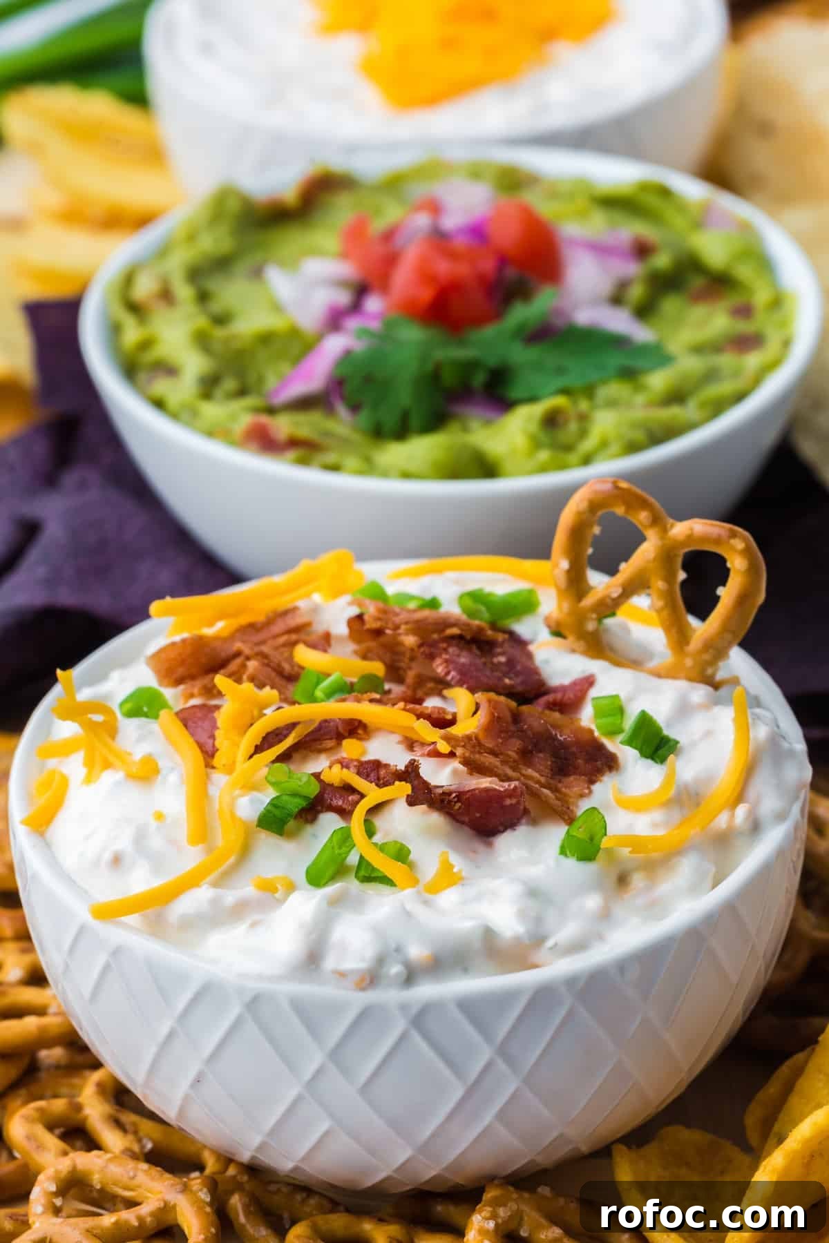Creamy Loaded Baked Potato Dip Recipe for Parties 2 A bowl of baked potato dip with a pretzel dipped on the side.