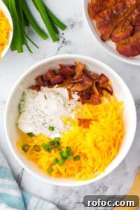 Creamy Loaded Baked Potato Dip Recipe for Parties 10 A white bowl featuring shredded cheese, bacon, ranch, and green onions.