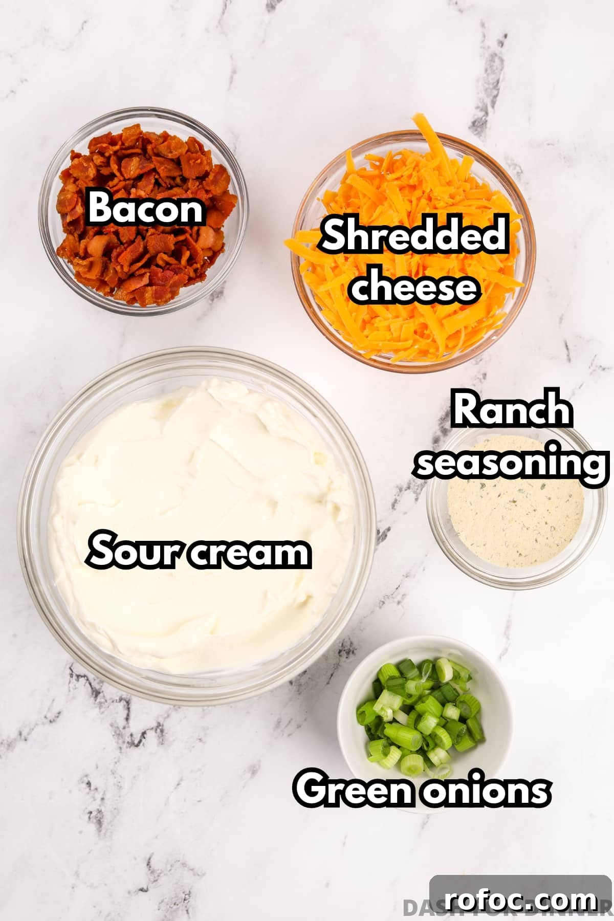 Creamy Loaded Baked Potato Dip Recipe for Parties 3 An overhead view of bowls of ingredients, including sour cream, shredded cheese, bacon, ranch seasoning, and green onions.