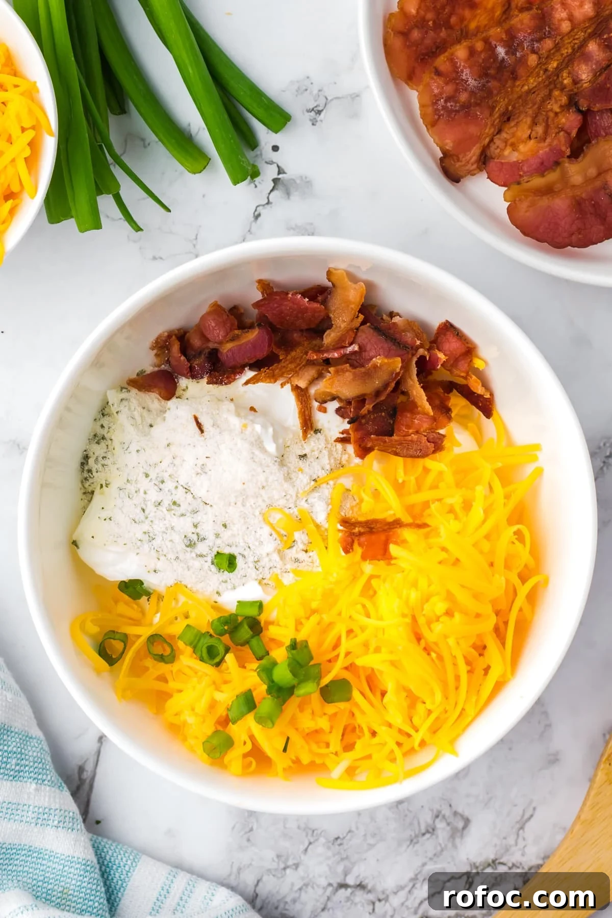 Creamy Loaded Baked Potato Dip Recipe for Parties 4 A white bowl featuring shredded cheese, bacon, ranch, and green onions.