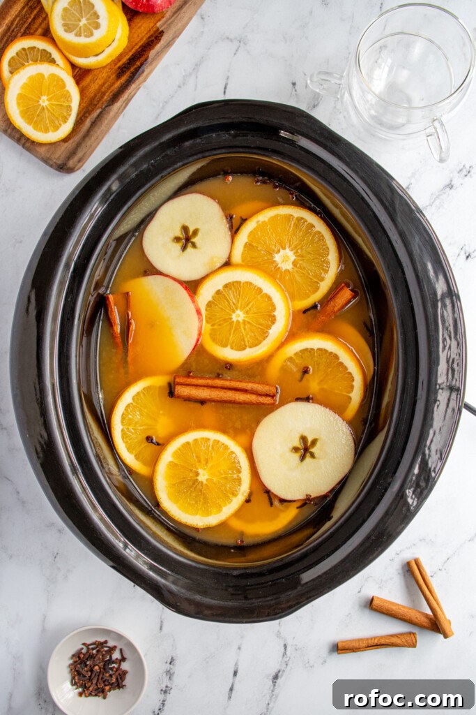 Slow-Cooker Christmas Wassail Recipe for Festive Parties 2 A black crockpot filled with Christmas wassail topped with apple and orange slices, cinnamon sticks, and cloves.