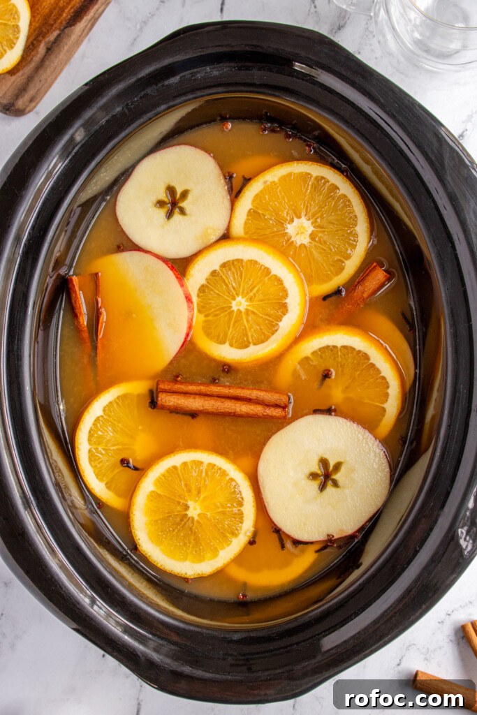 Slow-Cooker Christmas Wassail Recipe for Festive Parties 7 Crockpot filled with Christmas wassail and topped with orange slices, apples slices, cloves, and cinnamon sticks.
