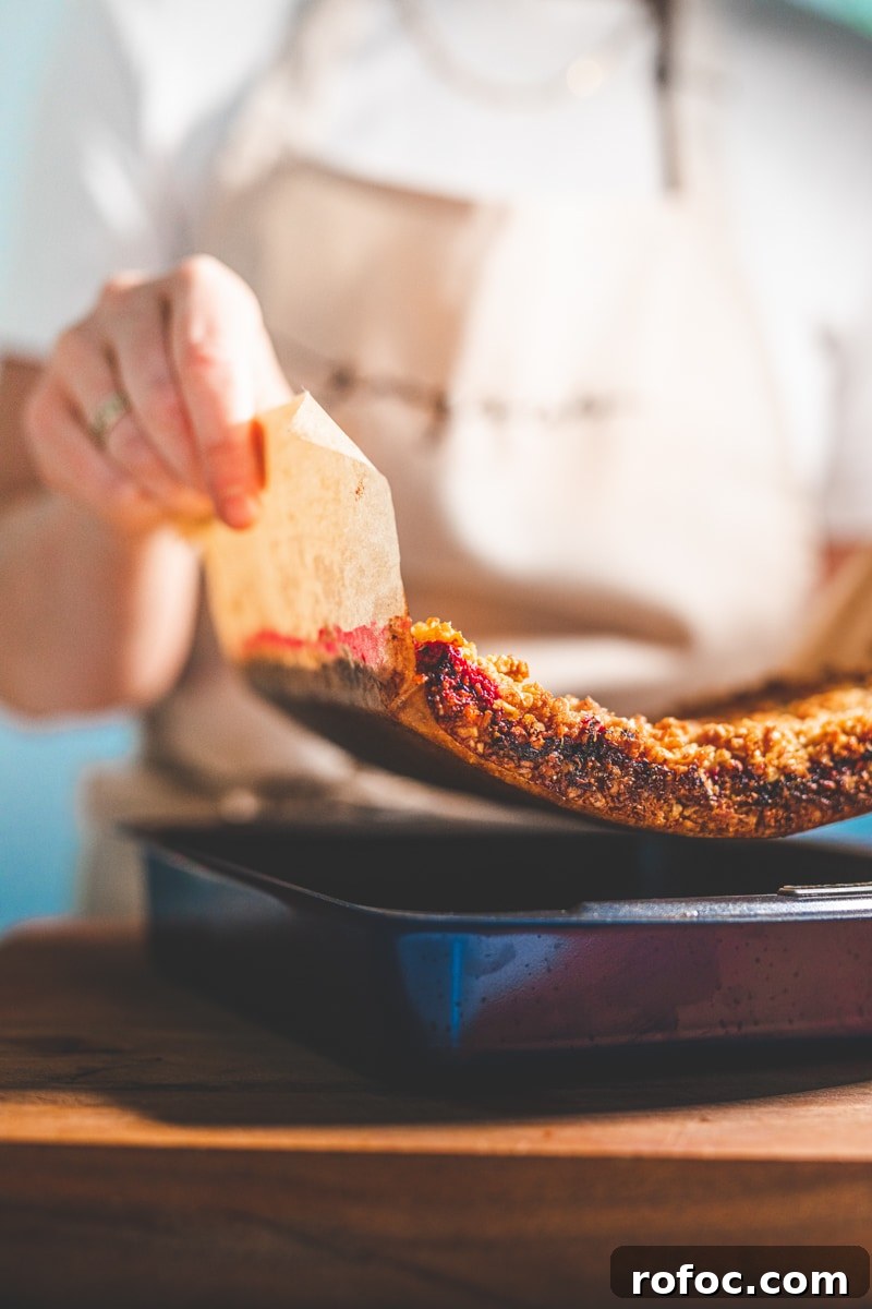 Coconut and Raspberry Flapjacks — Chewy Oat Bars Recipe 3 removing Coconut & Raspberry Flapjacks from tin - Georgie Eats