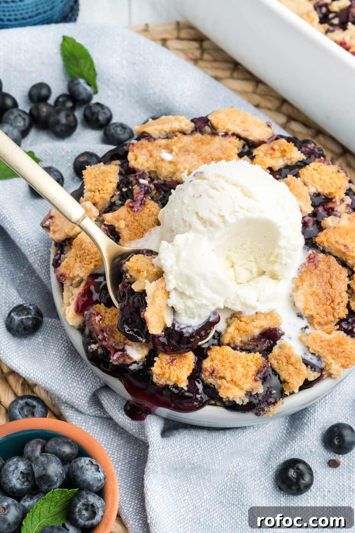 Blueberry Cake Mix Cobbler: Quick, Moist Dessert Recipe 2 Dish of blueberry cobbler with cake mix on the table with ice cream and a spoon taking a bite.