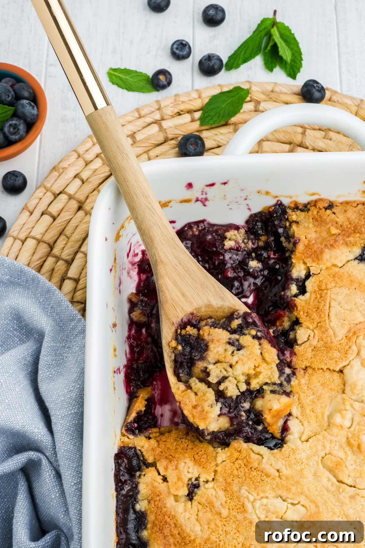 Blueberry Cake Mix Cobbler: Quick, Moist Dessert Recipe 7 Baked blueberry dump cake in casserole dish with a portion missing and a wooden spoon in it.
