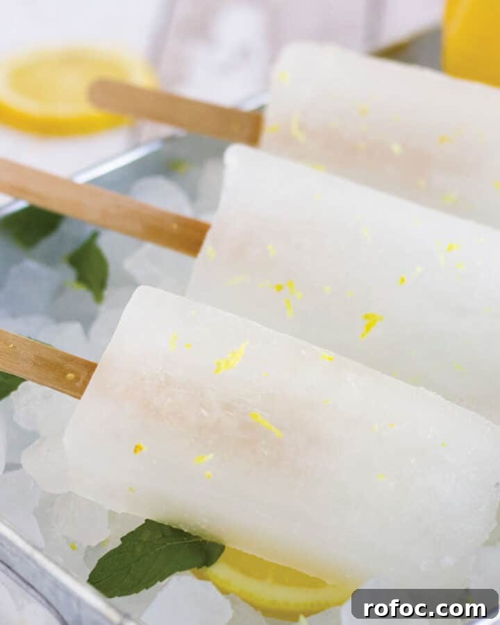 Three lemonade popsicles lying on ice with lemon slices and fresh mint.