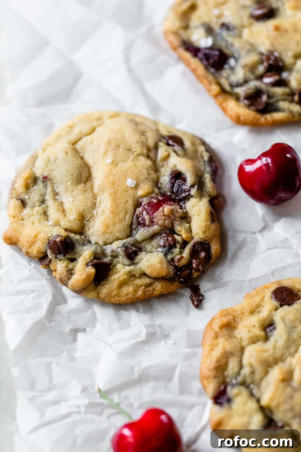 chocolate chip cookies on parchment paper with fresh cherries