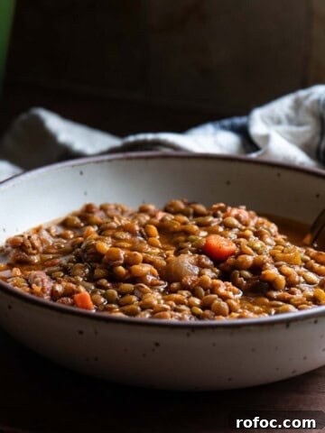 Lentil soup in a beige bowl with a spoon in it.