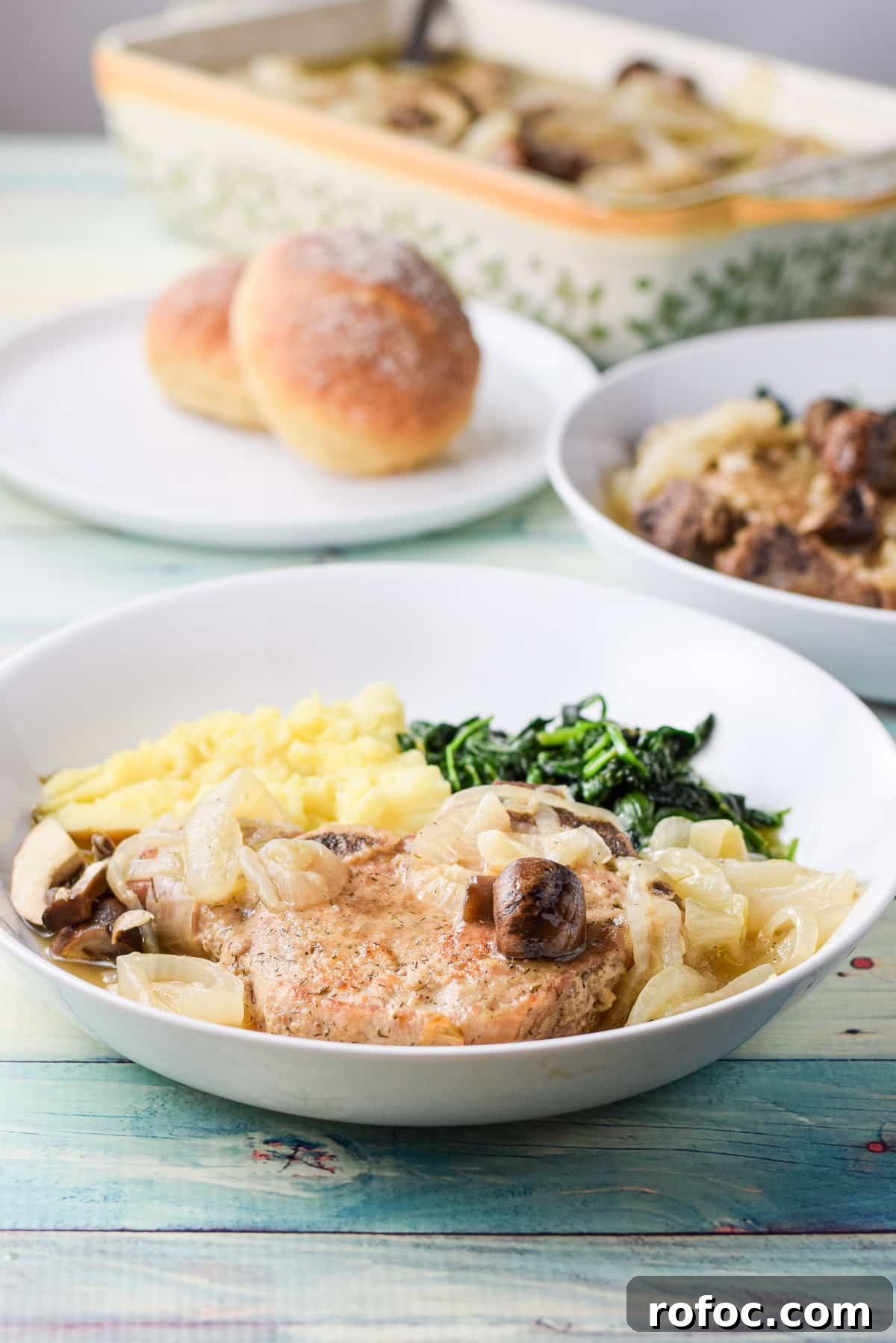 Juicy Pan-Seared Pork Chops with Garlic Butter Sauce 2 Pork chops in two white dishes with rolls and a casserole dish with the meat in back
