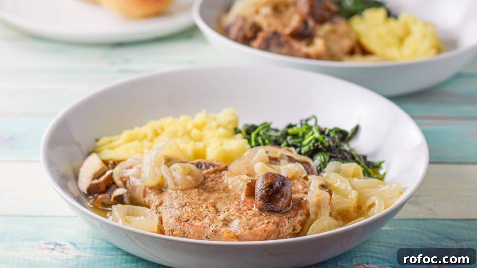 Juicy Pan-Seared Pork Chops with Garlic Butter Sauce 3 A deep plate with a pork chop with mushrooms, onions and a sauce along with a potato and spinach
