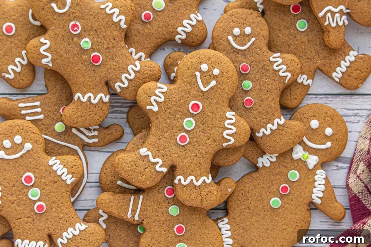Gingerbread Cutout Cookies: Classic Spiced Cookie Recipe for Decorating 4 Christmas gingerbread cut out cookies decorated with white icing and red and green buttons, stacked on a wooden background.