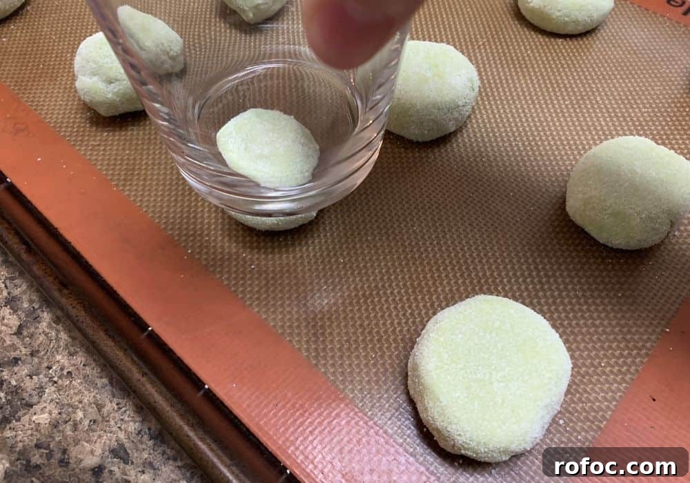 Zesty Lime Jello Sugar Cookie Recipe for Bright, Chewy Cookies 7 balls of lime jello cookie dough rolled in sugar and being flattened slightly with the bottom of a drinking glass