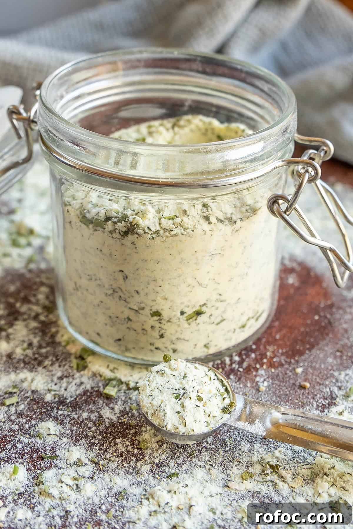 Homemade Ranch Seasoning Mix Recipe for Dip, Dressings & Marinades 2 A glass jar filled with powdered seasoning is surrounded by a scattered layer of the same mixture. A measuring spoon holds some of the seasoning in front of the jar.
