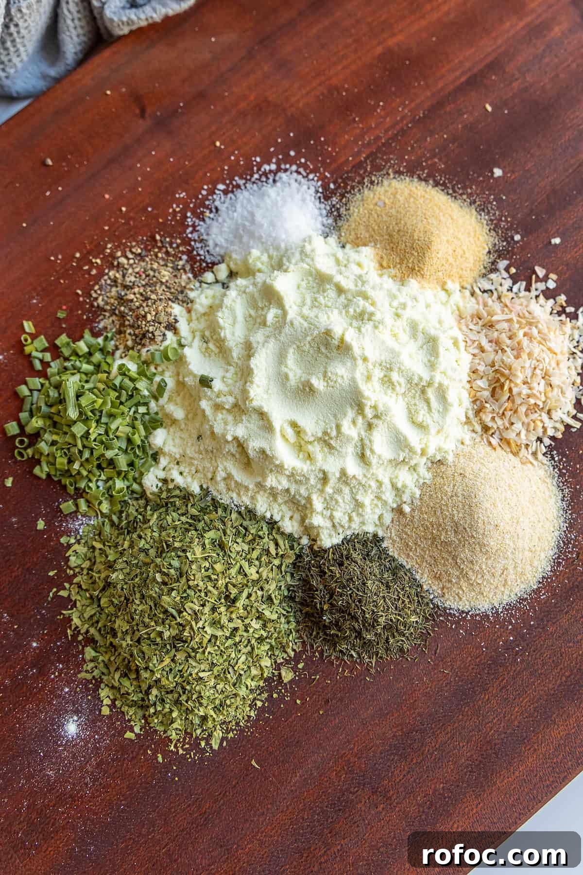 Homemade Ranch Seasoning Mix Recipe for Dip, Dressings & Marinades 5 Assorted spices and herbs, including green herbs, yellow powders, and salt, are arranged in piles on a wooden surface.
