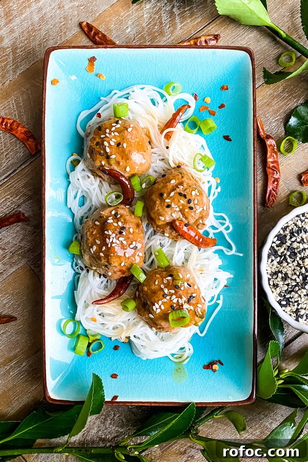 4 spicy General Tso's meatballs on a plate with rice noodles