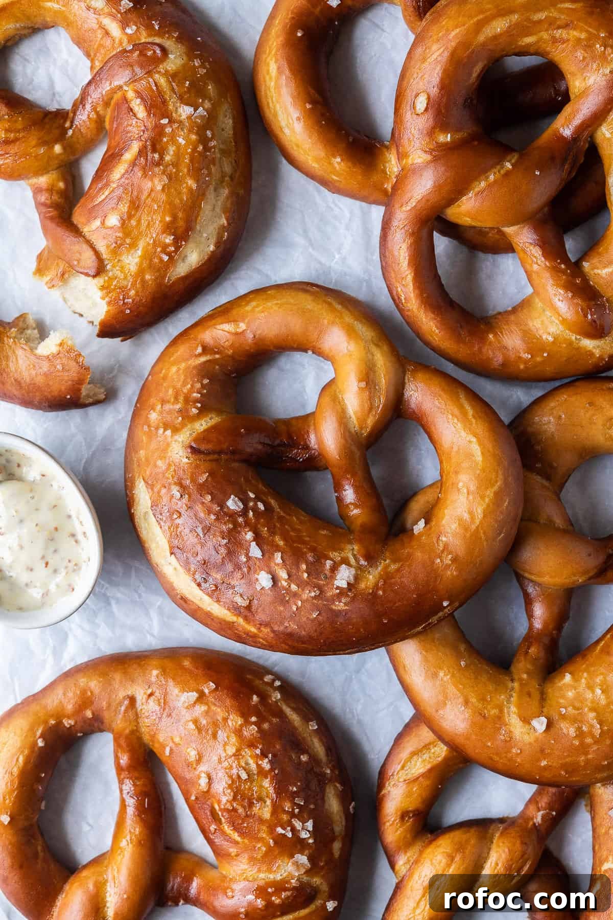 Vegan beer pretzels - these delicious vegan soft pretzels are made with (optional) beer to give them extra flavour. They are super soft, flavourful and easier to make than you might think! #veganbread #veganbaking #eggless #dairyfree Pretzels on a sheet of white baking parchment.