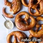 Vegan Soft Beer Pretzels Recipe for Chewy, Flavorful Snacks 7 Vegan beer pretzels on a sheet of white baking parchment with a bowl of mustard sauce.