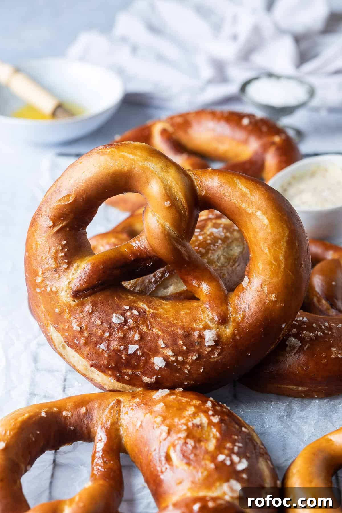 Vegan beer pretzels - these delicious vegan pretzels are made with (optional) beer to give them extra flavour. They are super soft, flavourful and easier to make than you might think! #veganbread #veganbaking #eggless #dairyfree Close up of a vegan beer pretzel on a wire rack with a bowl of melted butter and a brush.