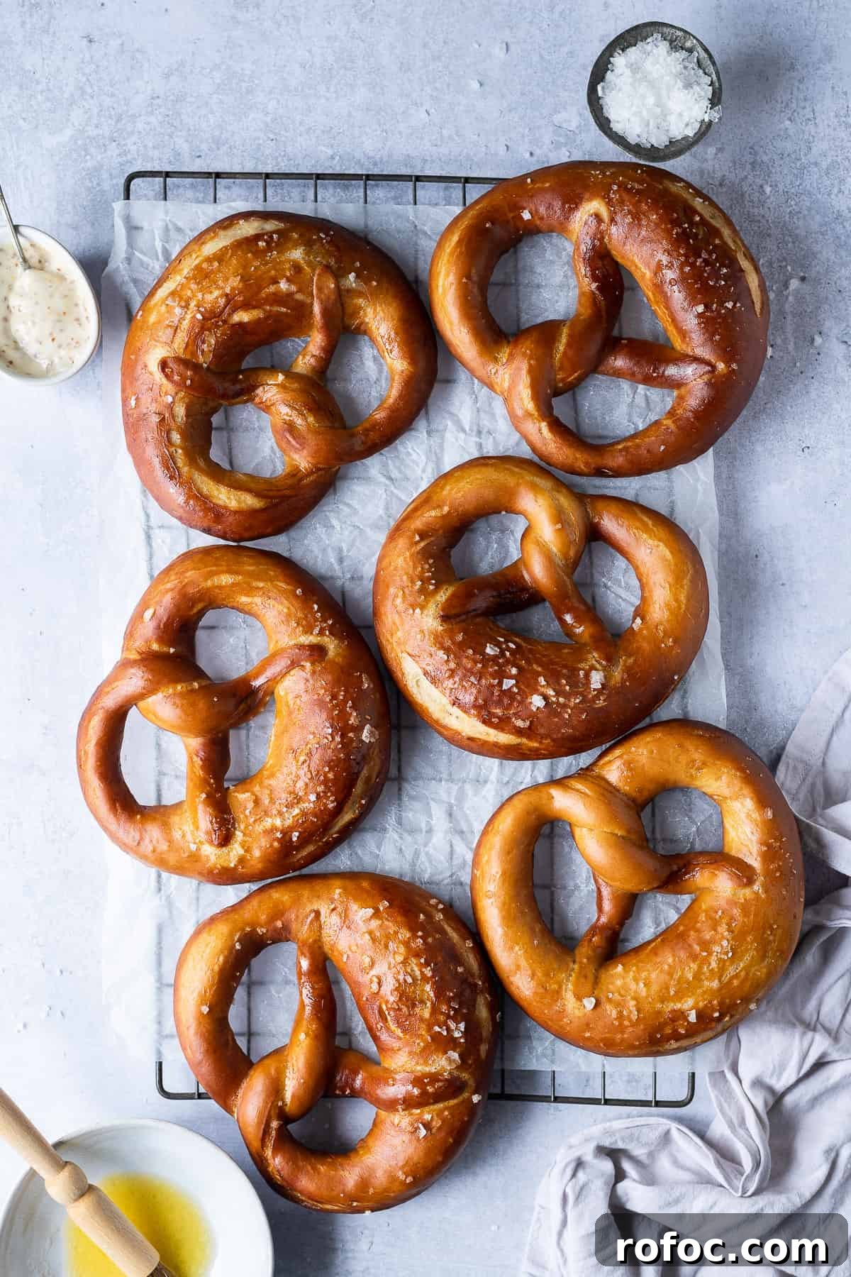 Vegan beer pretzels - these delicious vegan pretzels are made with (optional) beer to give them extra flavour. They are super soft, flavourful and easier to make than you might think! #veganbread #veganbaking #eggless #dairyfree Vegan pretzels on a wire rack on a grey background.
