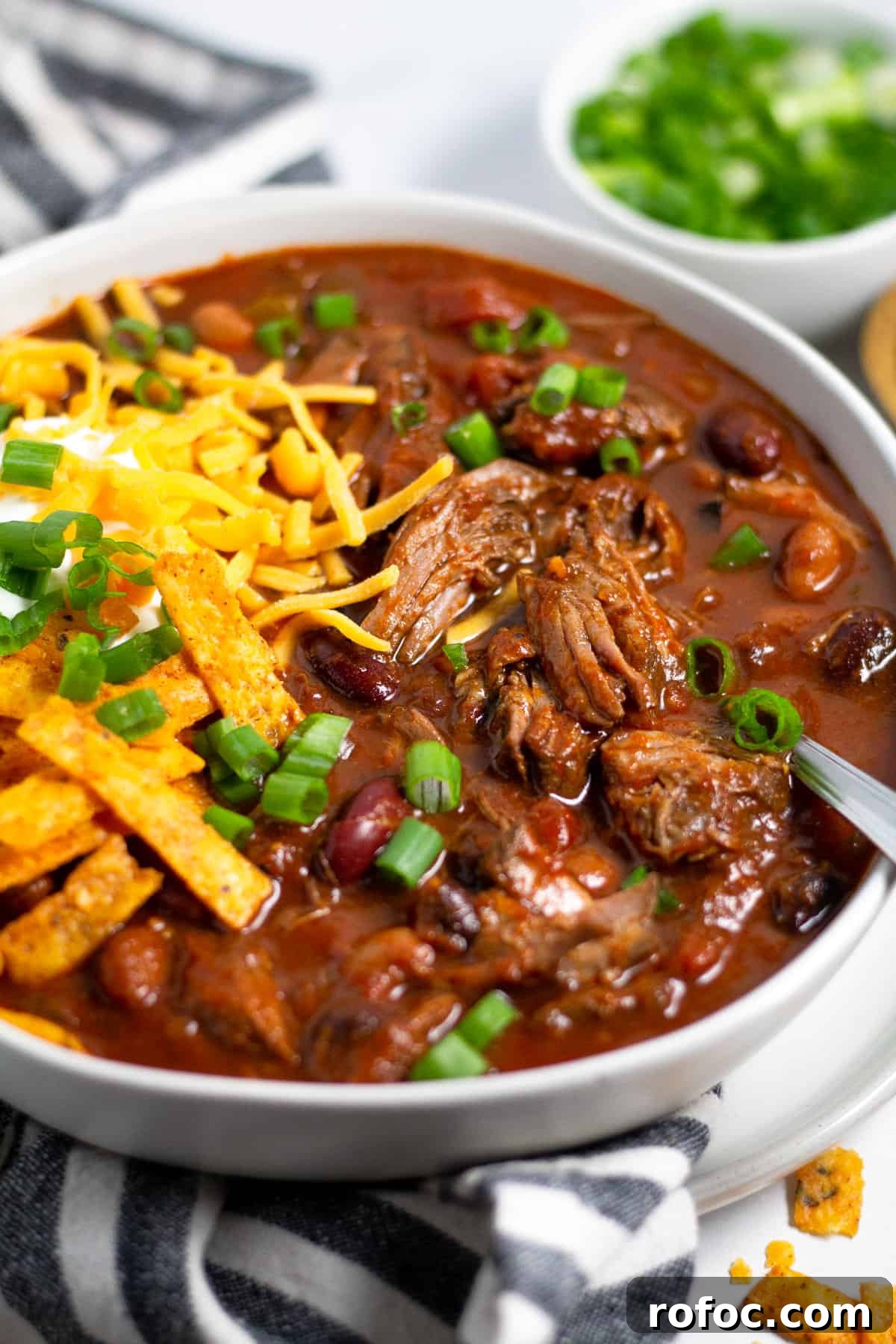 Close up shot of a bowl of short rib beef chili topped with sour cream and cheese