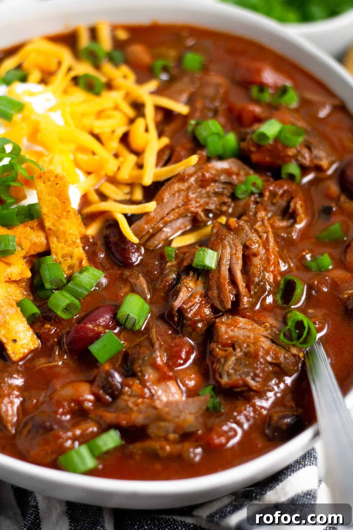 Close up shot of a bowl of short rib beef chili topped with sour cream and cheese