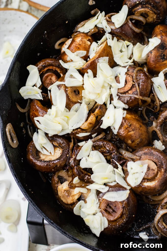 Creamy Mascarpone Garlic Mushrooms with Herbs and Toasted Bread 5 A cast iron skillet of sautéed mushrooms with sliced garlic sitting on top of the mushrooms.