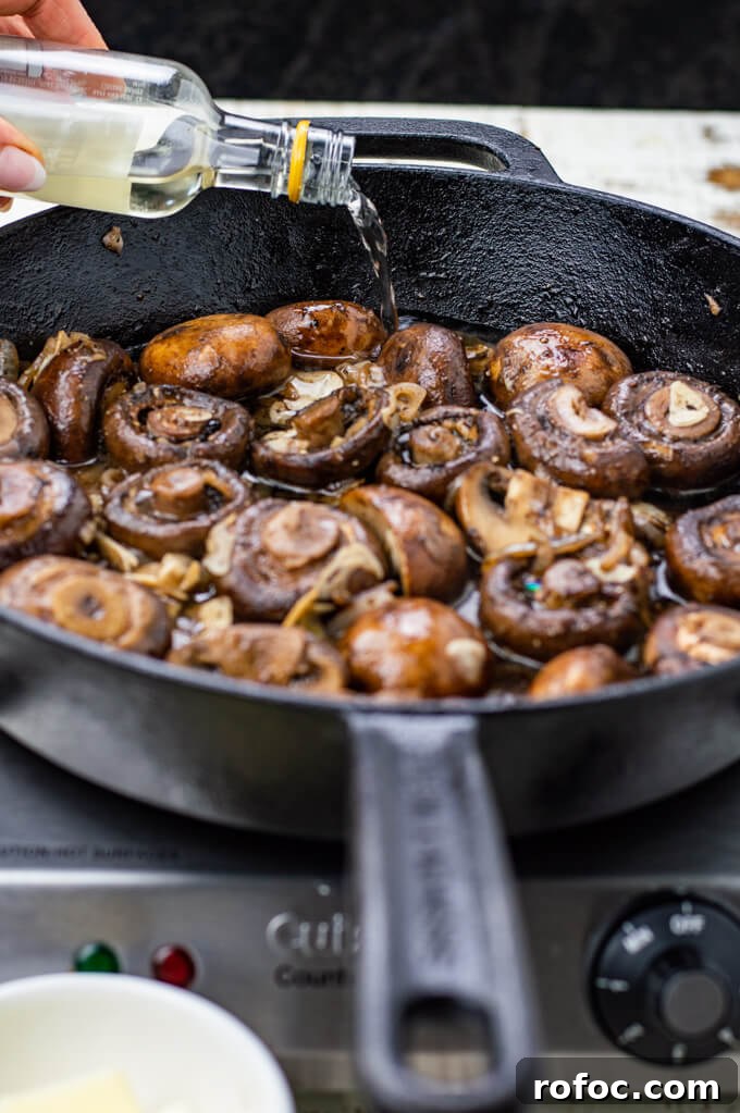 Creamy Mascarpone Garlic Mushrooms with Herbs and Toasted Bread 6 Sautéed mushrooms are in a cast iron skillet with a bottle of wine being poured into the mushrooms.