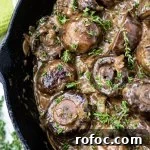 A close-up photo of sautéed mushrooms in a creamy sauce with chopped thyme sprinkled on top. All of this is in a cast iron skillet.