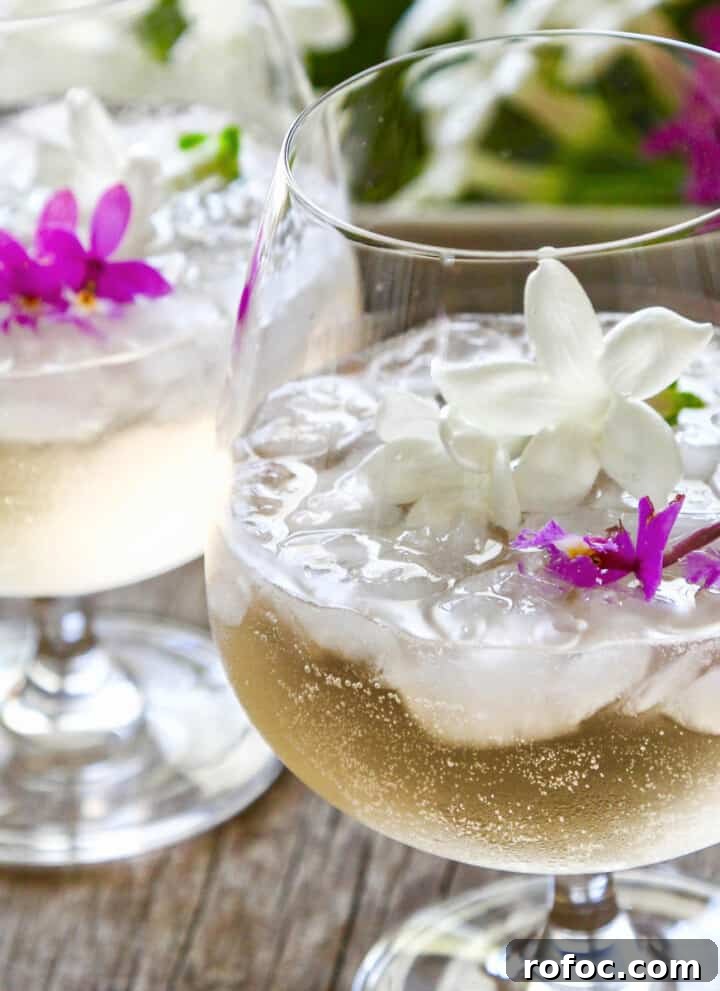 Two glasses filled with St Germain cocktails garnished with tiny purple orchids and white jasmine flowers.