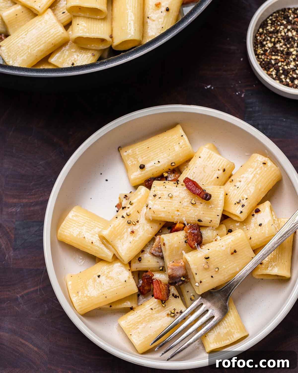 Rigatoni alla Gricia Recipe: Classic Roman Pork-Bacon Pasta 8 White plate with rigatoni alla gricia on walnut cutting board.