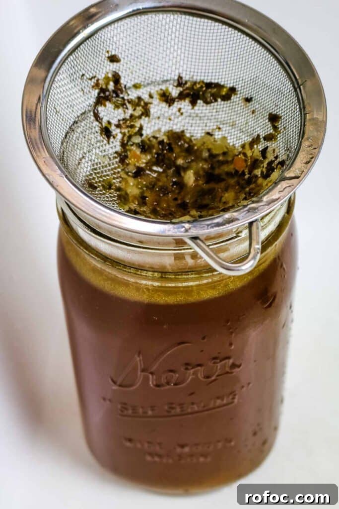 Rich Homemade Beef Bone Broth Recipe for Deep Flavor and Nutrition 13 running broth through sieve in mason jar.