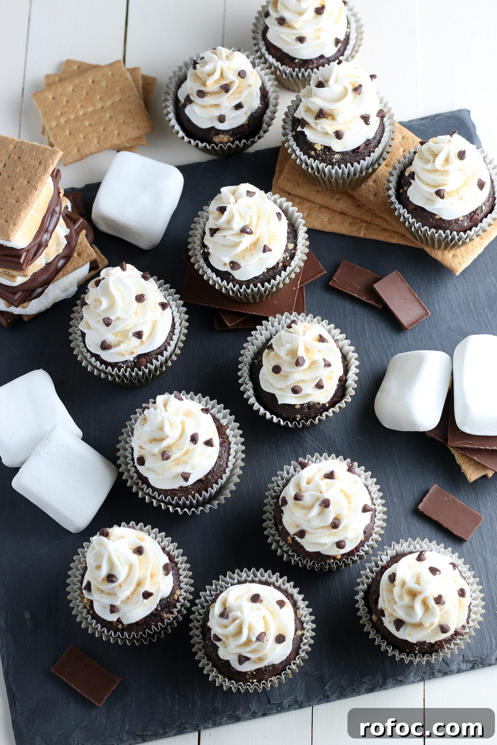 finished s'more cupcake recipe with cake mix with graham crackers, chocolate, and marshmallows on a grey cutting board.
