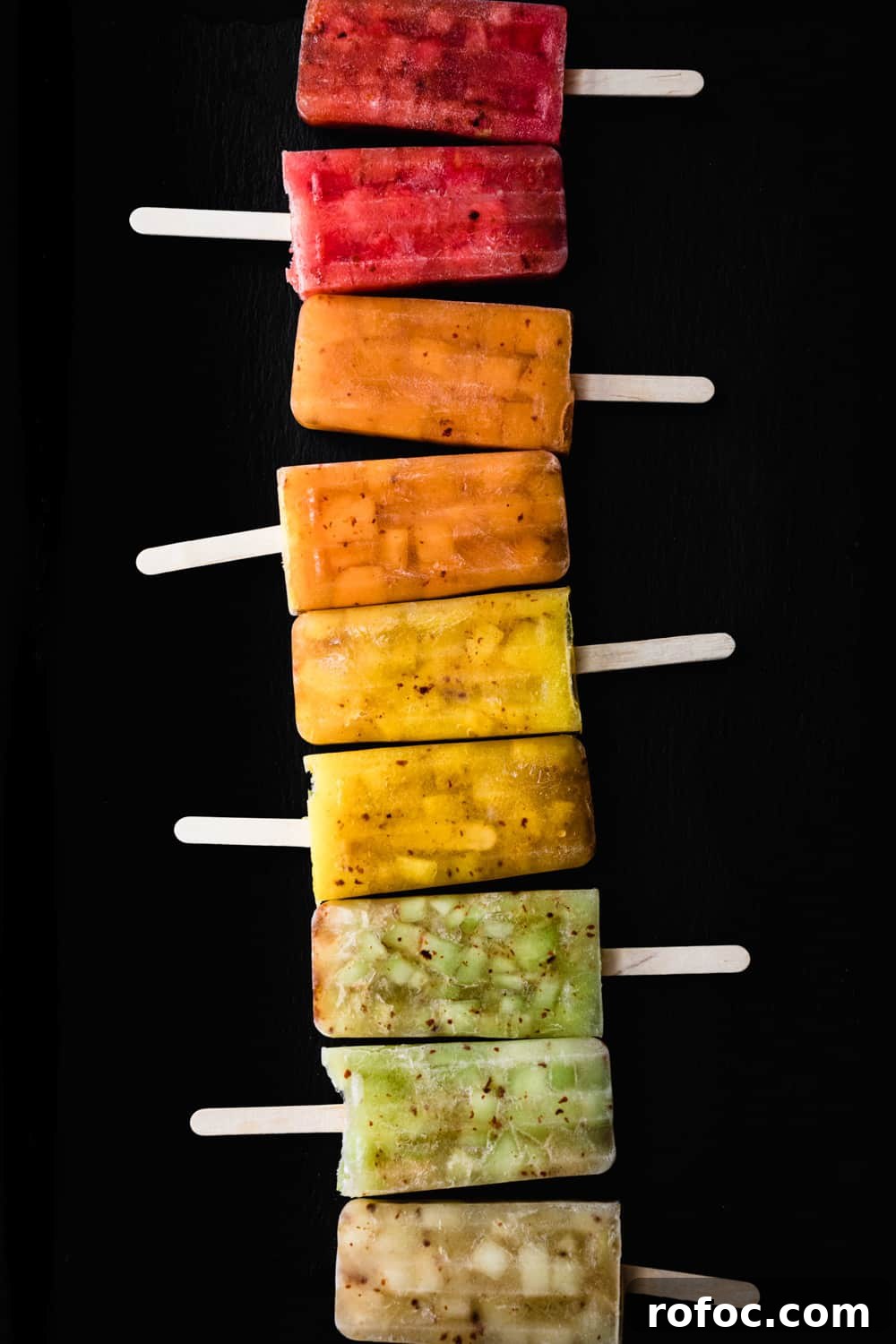 Spiced Watermelon Popsicles: Vibrant, Refreshing Summer Treat 3 a popsicles rainbow! Red, pink, orange, yellow, green and white melon and chile popsicles lined like a rainbow; overhead shot on a black background
