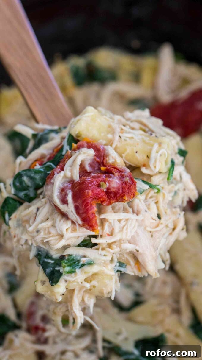 Tuscan Chicken Pasta Made in a Slow Cooker: Creamy One-Pot Meal 4 a serving spoon of Crockpot Tuscan pasta with shredded chicken and cheese