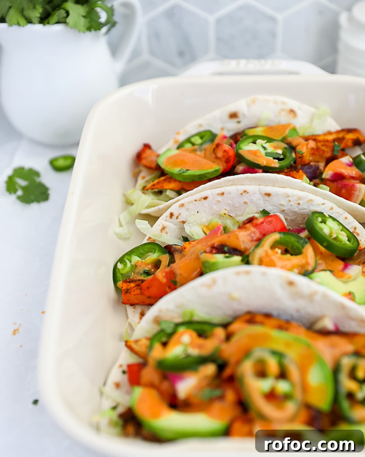 Flavor-Packed Veggie Tacos: Fresh Recipes for Every Night 5 Three tacos in a white dish with fresh vegetables and an orange sauce.
