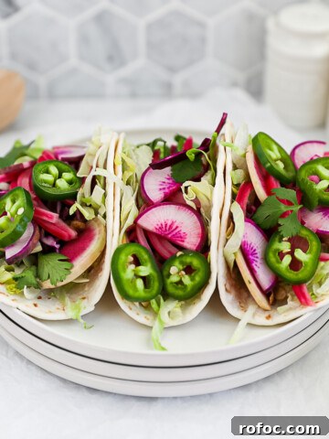 Three vegetable tacos on a stack of white plates filled with fresh vegetables.