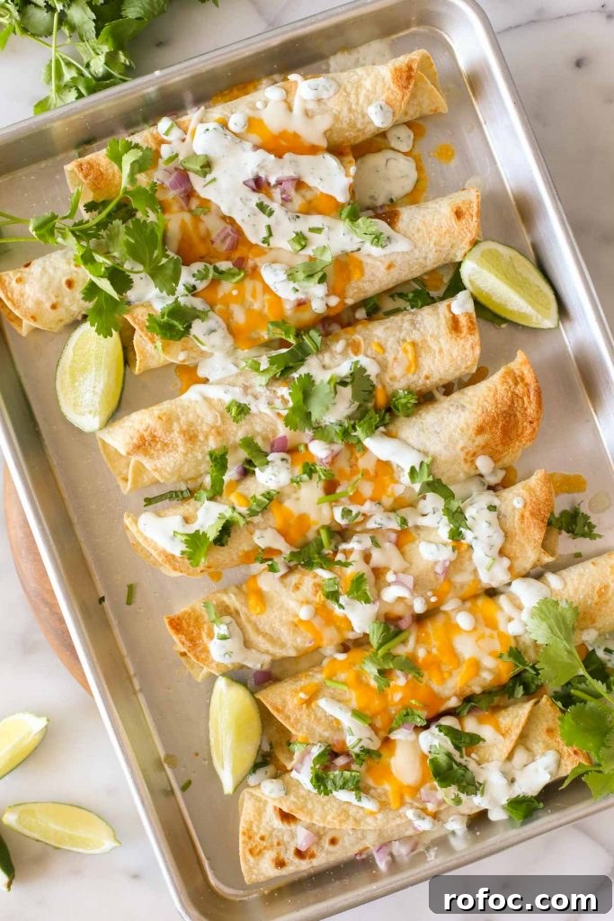 BBQ Chicken Taquitos with Cilantro-Lime Cream Sauce 2 Overhead shot of BBQ Chicken Taquitos on a baking sheet, garnished with lime wedges and fresh cilantro.