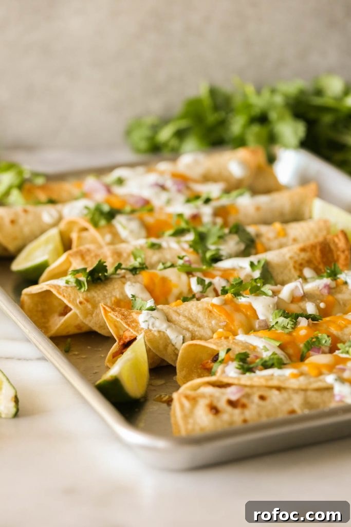 BBQ Chicken Taquitos with Cilantro-Lime Cream Sauce 5 BBQ Chicken Taquitos garnished with fresh cilantro and lime wedges on a baking sheet.