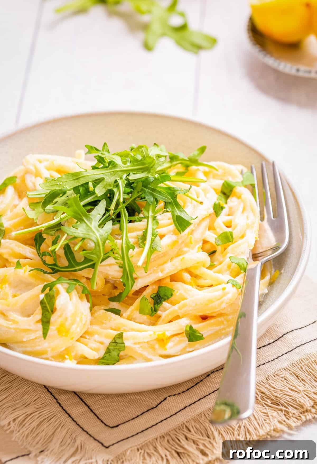 Creamy Lemon Ricotta One-Pot Pasta Recipe 2 Close-up view of one pot lemon ricotta pasta topped with chopped basil and rocket leaves placed on a plate with a fork on the side.