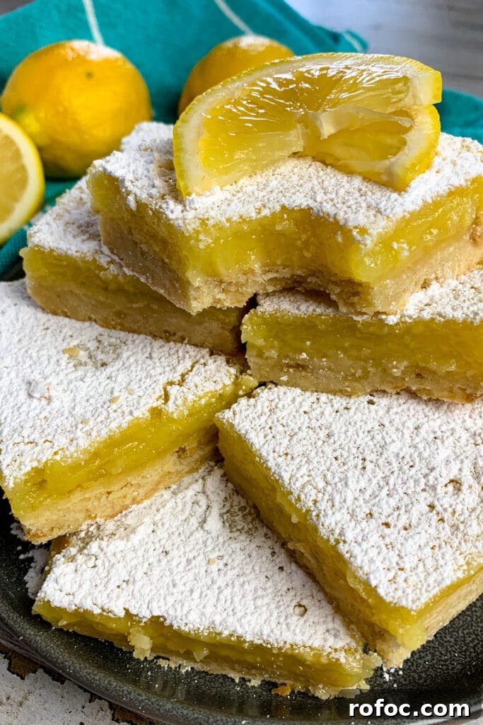 Zesty Lemon Bars Recipe: Bright, Tangy Dessert Bars 4 Lemon bars are stacked up on a plate and garnished with a sliced lemon.