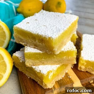 Zesty Lemon Bars Recipe: Bright, Tangy Dessert Bars 5 Lemon bars stacked up on a wood cutting board.