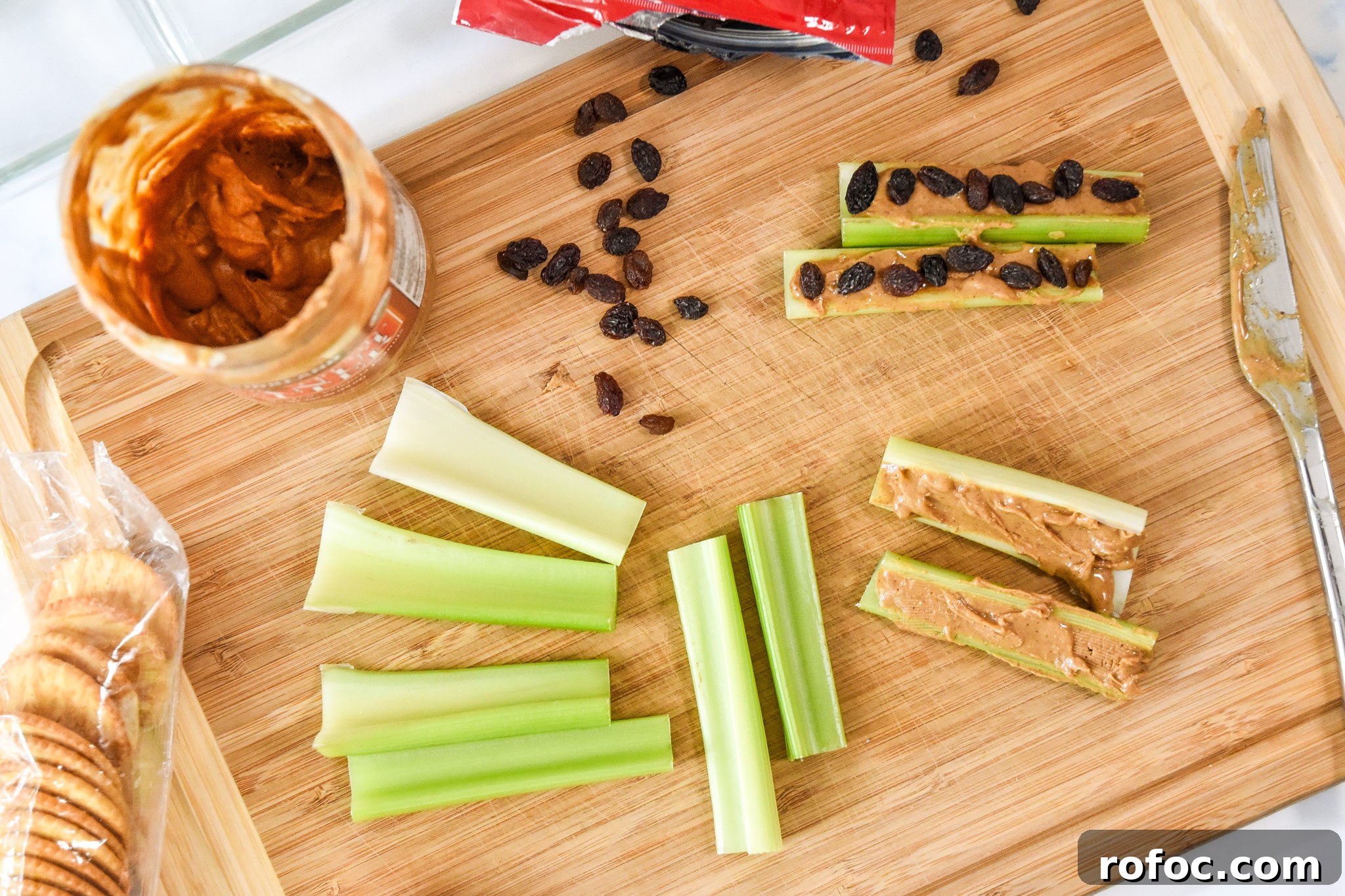 assembling ants on a log with celery, peanut butter and raisins on a cutting board.