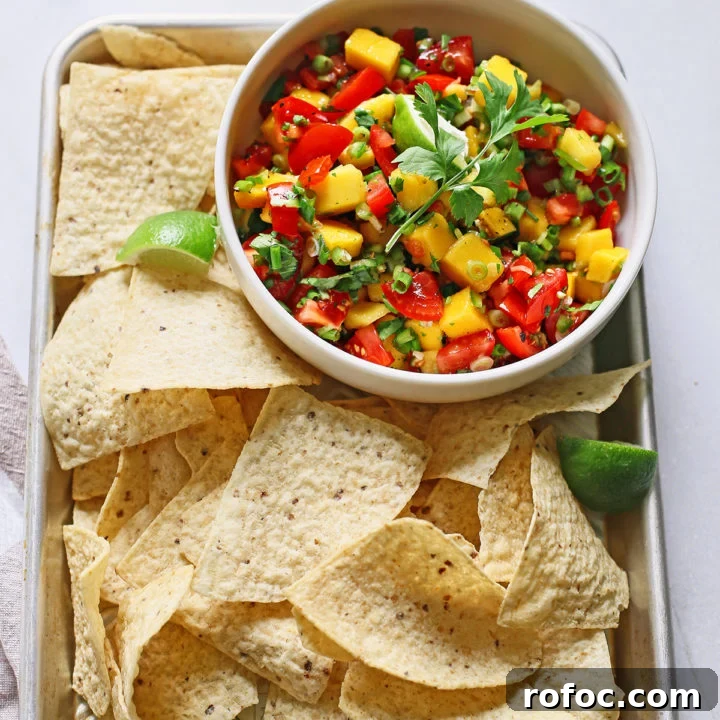 fresh mango salsa in a white bowl surrounded by tortilla chips on a metal tray