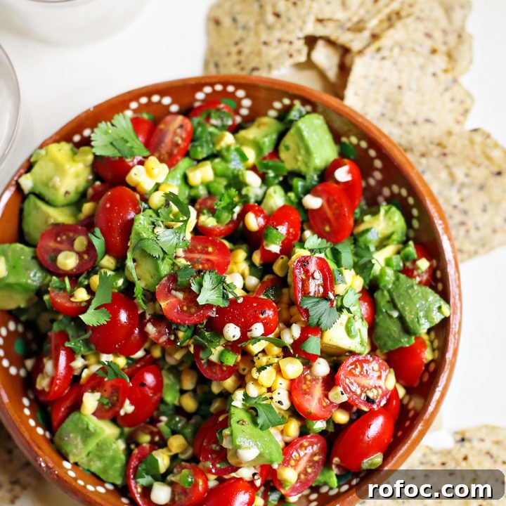 tomato avocado corn salad in a red bowl surrounded by tortilla chips