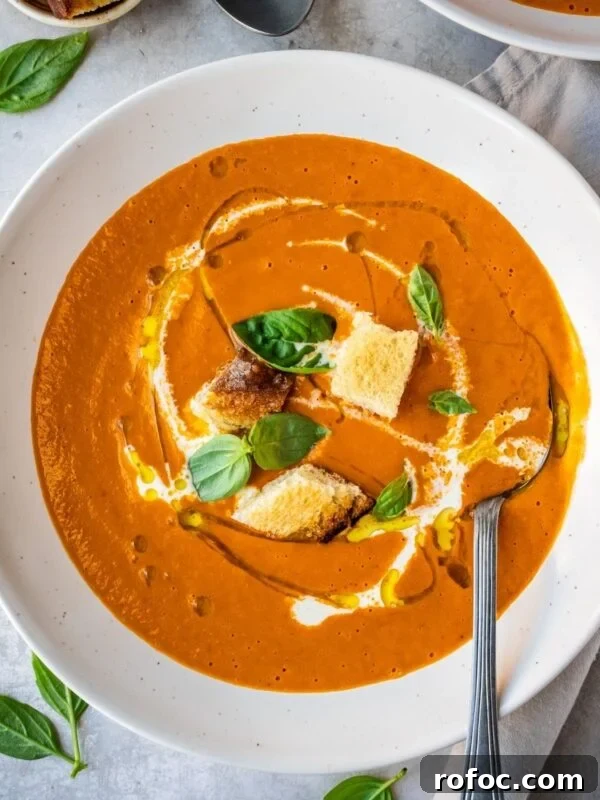 Roasted red pepper and tomato soup in a bowl, garnished with croutons, fresh basil, olive oil and cream.