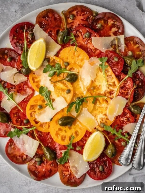 Large platter with sliced heirloom tomato carpaccio with shaved parmesan, arugula, capers and caper berries.