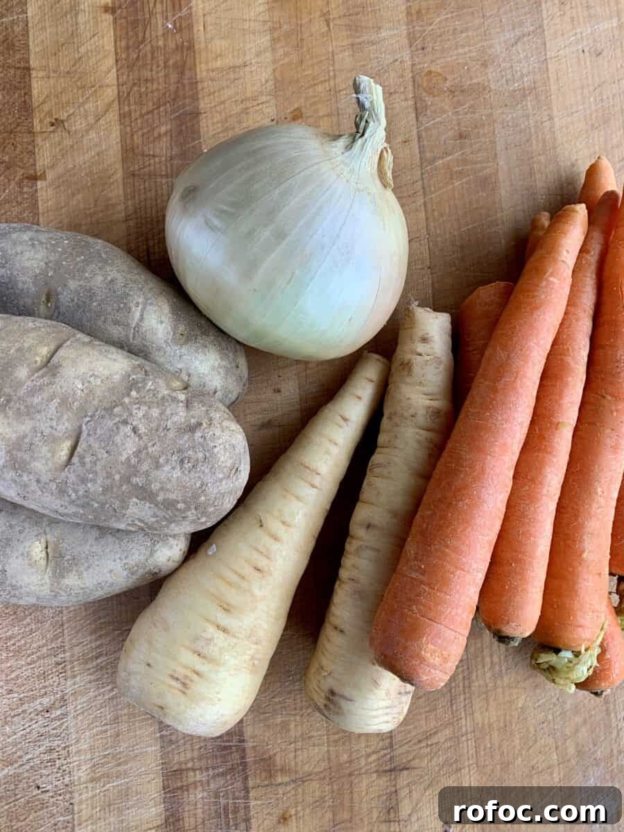 Traditional Irish Beef Stew Recipe for Hearty Weeknight Dinners 3 Potatoes, onion, parsnips and carrots on a cutting board.