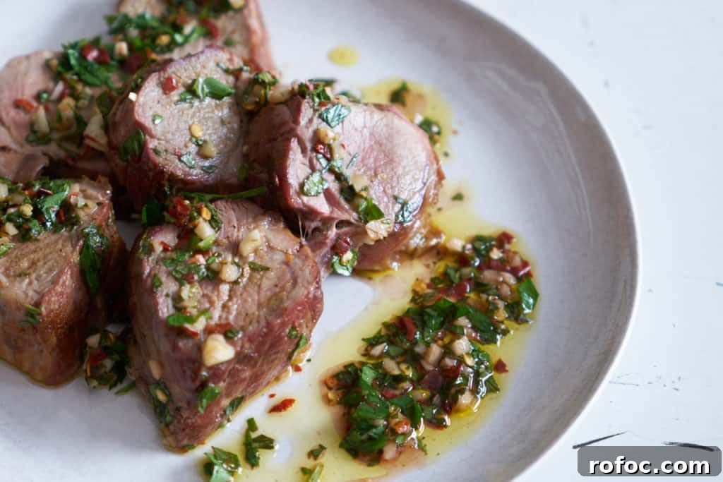 Grilled Pork Tenderloin with Fresh Chimichurri Sauce 2 Slices of grilled pork tenderloin with chimichurri sauce on a white plate.