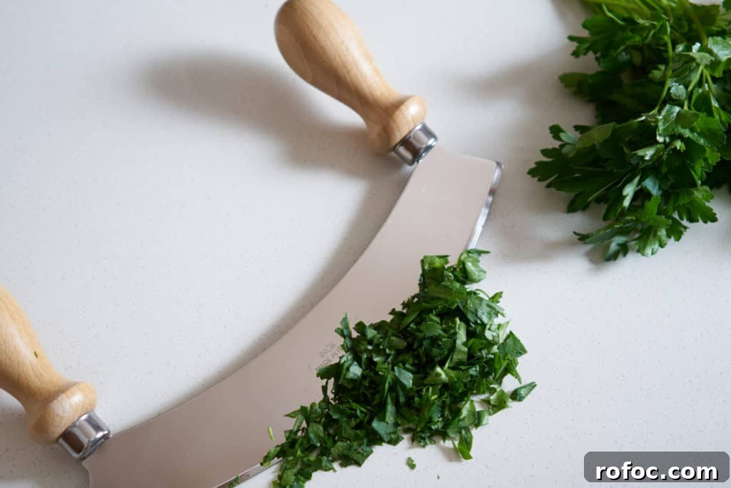 Grilled Pork Tenderloin with Fresh Chimichurri Sauce 4 A mezzaluna with wooden handles, chopped parsley, and a bundle of fresh parsley on a white surface.