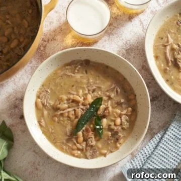 A Dutch oven and two bowls of pork stew, two glasses of beer, some fresh sage, and a blue napkin.
